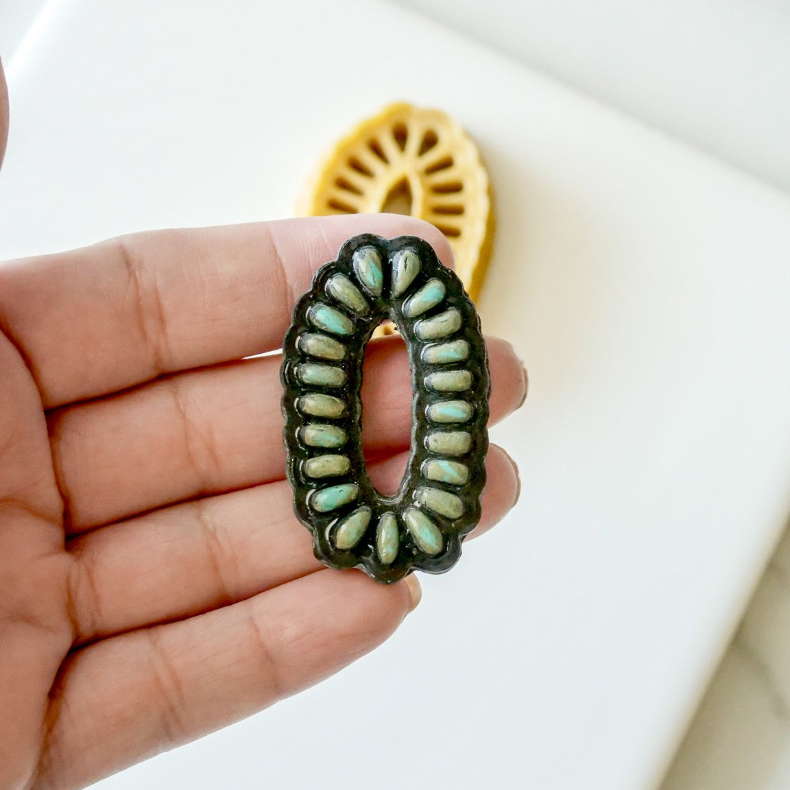 Hand holding a green Oblong Faux Stone with a blurred background