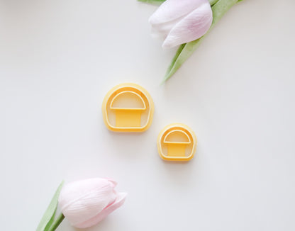 Two pastel pink tulips with green stems frame two yellow, mushroom-shaped Hello Cutters Basket Polymer Clay Cutter STL Set pieces in different sizes on a white background—ideal for a unique digital download.
