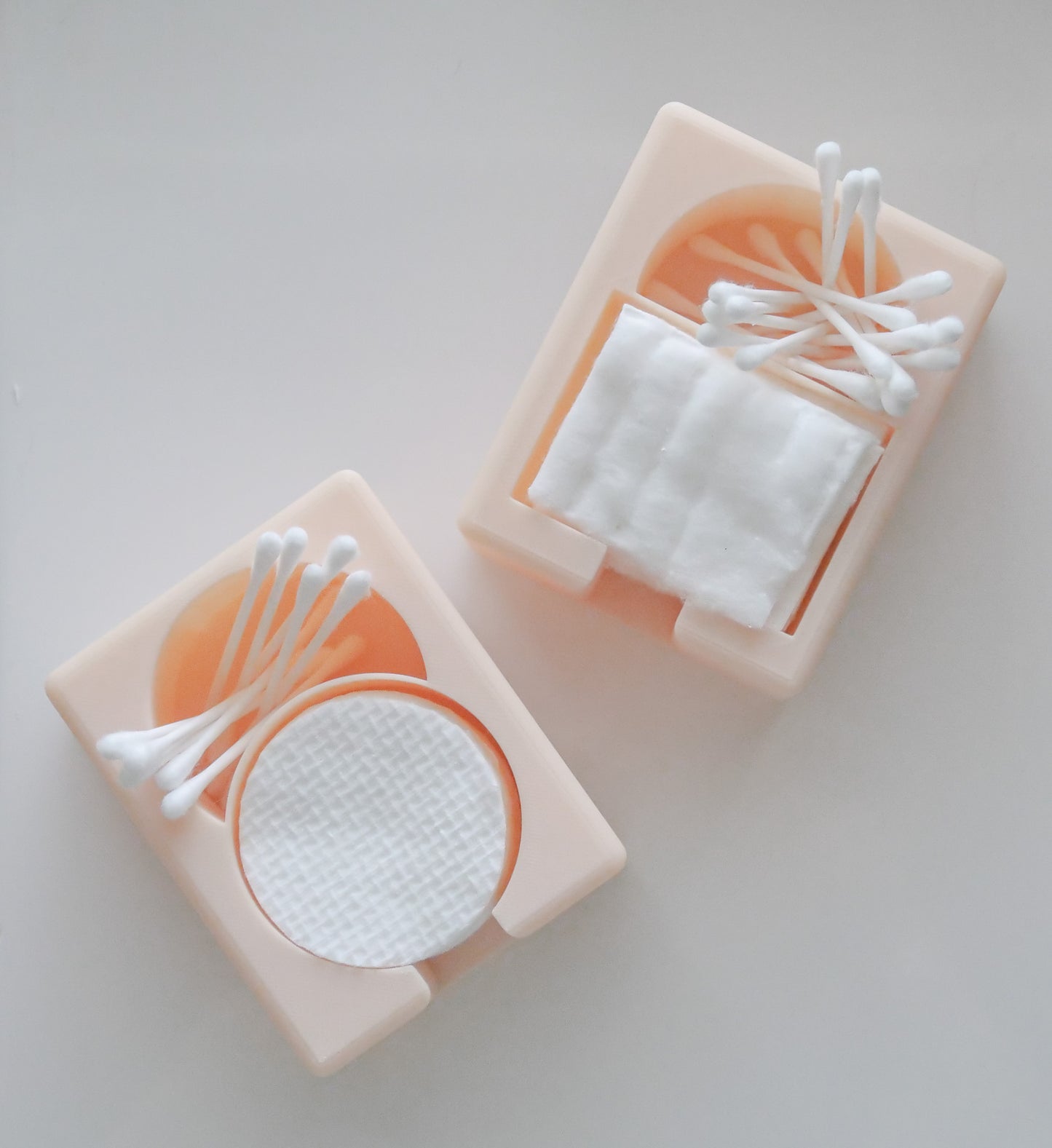 The Hello Cutters Round Cotton Holder Duo, in beige, organizes cotton pads and Q-tips—one holder contains round pads, while the other holds square pads with Q-tips on top—displayed on a white surface.