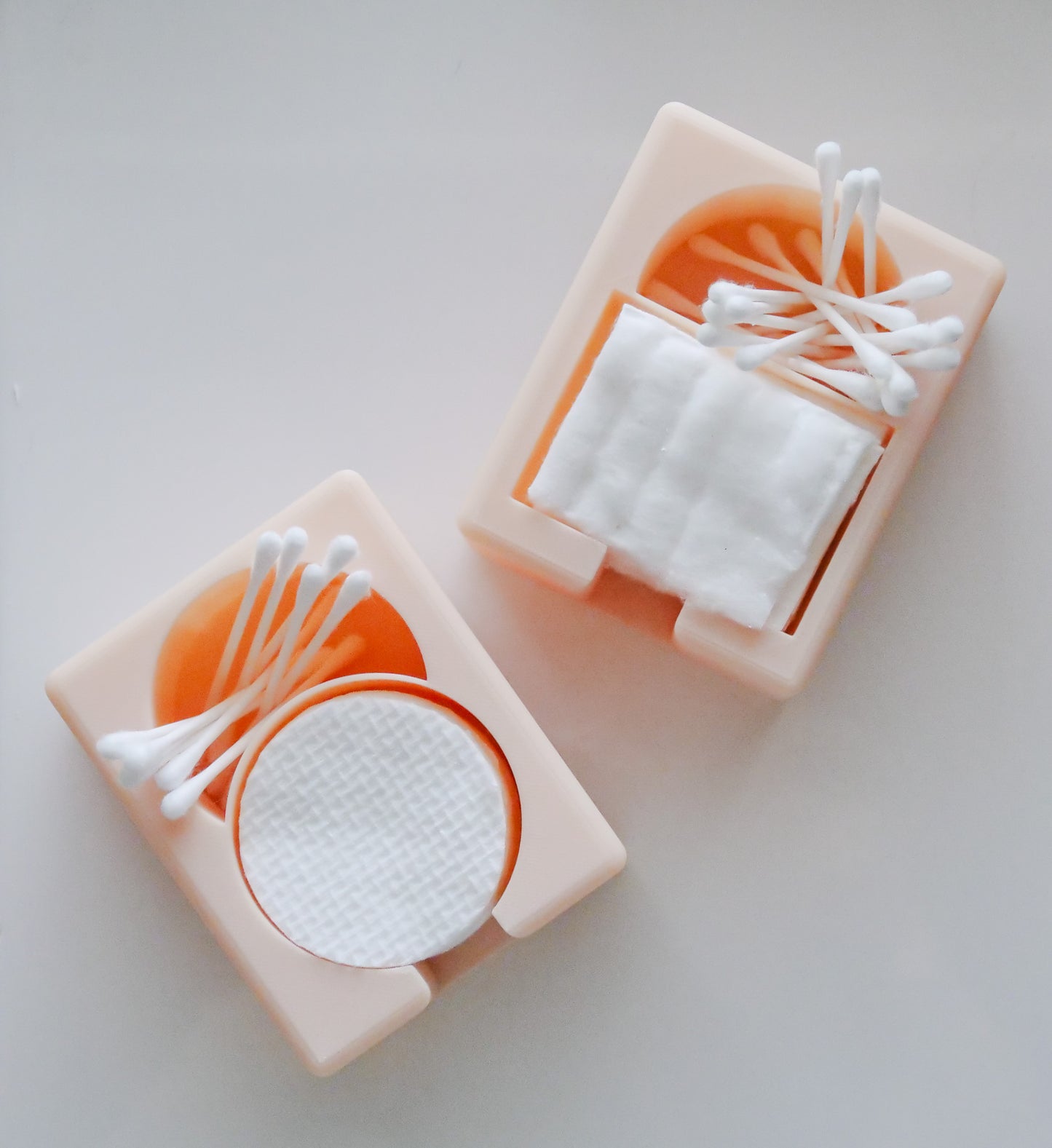 The Hello Cutters Rectangle Cotton Holder Duo features two peach containers: one for round cotton pads, the other for square ones, each topped with neatly arranged Q-tips. Their minimalist design stands out against a white backdrop—ideal for 3D print fans.
