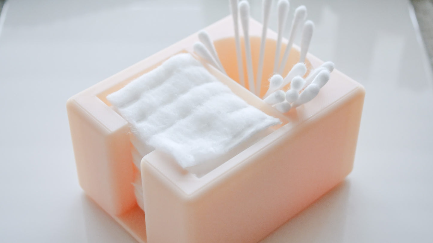 The Hello Cutters Rectangle Cotton Holder Duo, a pink plastic organizer for cotton pads and Q-tips, is displayed on a smooth, white surface.