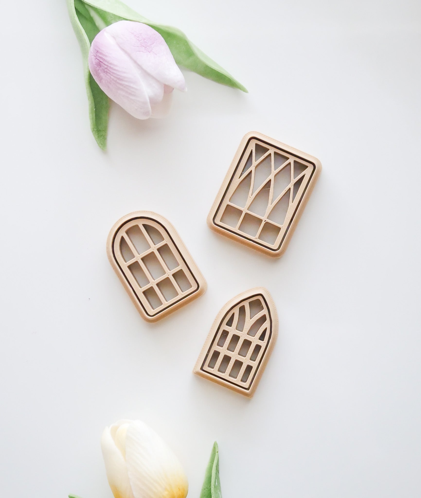 Three window-shaped polymer clay cutters from the Window Polymer Clay Cutter Set by Hello Cutters are displayed on a white background with two artificial tulips—pink above and yellow below—inspiring your next 3D printable project.