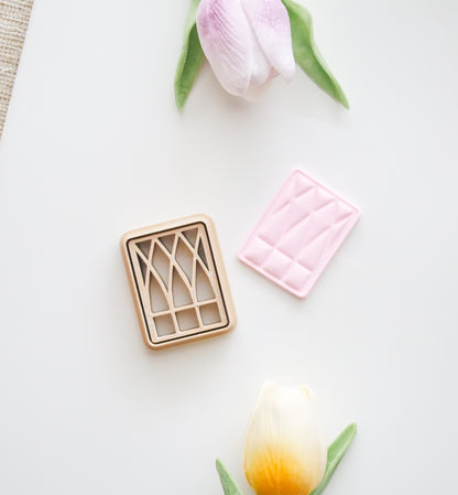 The Window Polymer Clay Cutter Set by Hello Cutters, a pink fondant piece with a matching design, and two artificial tulips—one pink, one yellow—are displayed on a white surface beside the 3D printable STL file.