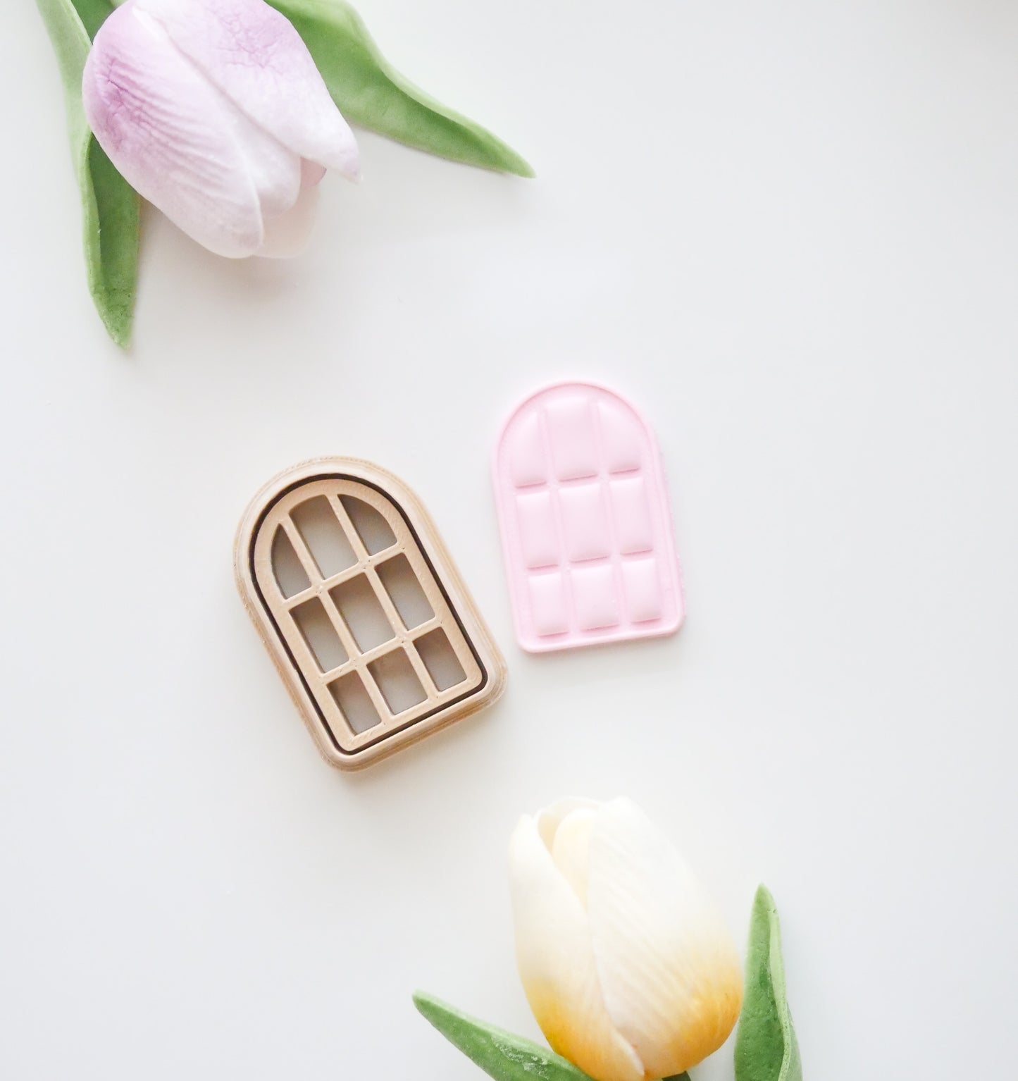 The Hello Cutters Window Polymer Clay Cutter Set, featuring a plastic arched window-shaped cutter and matching pink dough imprint, is displayed with two pastel tulips on a white background.