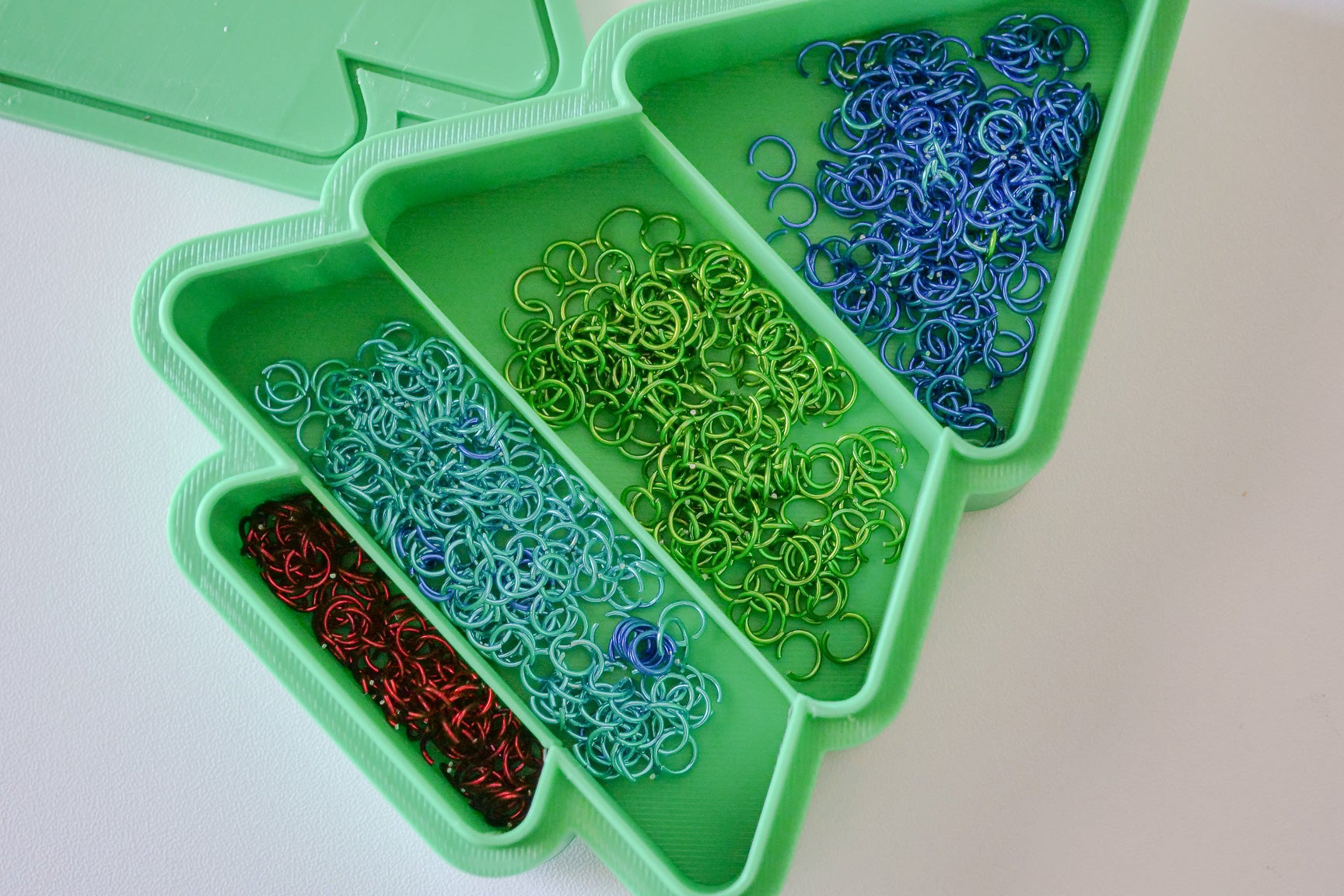Green organizer tray with compartments filled with colorful rubber bands on a light background